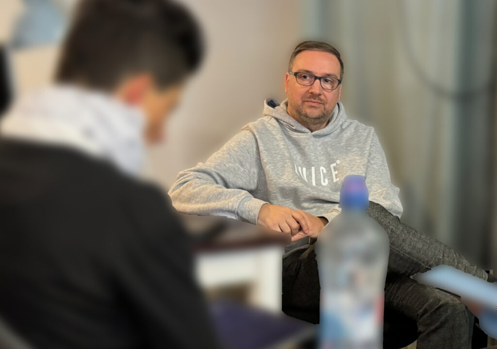 André sitzt an einem Tisch und hört konzentriert einem Coachee zu.