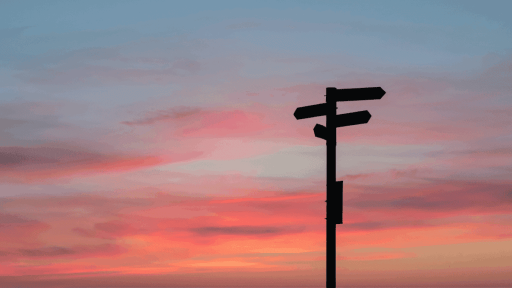 Ein rötlich gefärbter Himmel. Davor die Schattensillhouette eines Wegweisers mit Pfeilen in verschiedene Richtungen